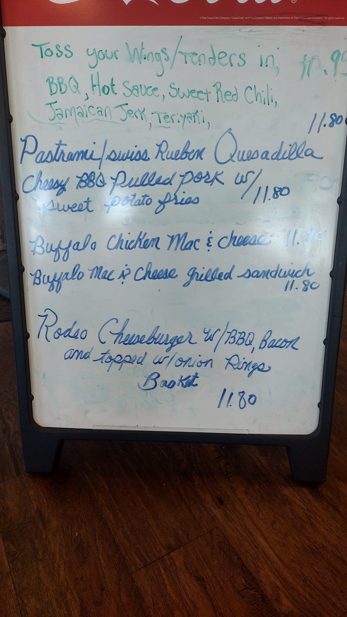 A handwritten specials board listing wing and tender sauces, a pastrami Reuben quesadilla, BBQ pulled pork, buffalo chicken mac and cheese and a rodeo cheeseburger