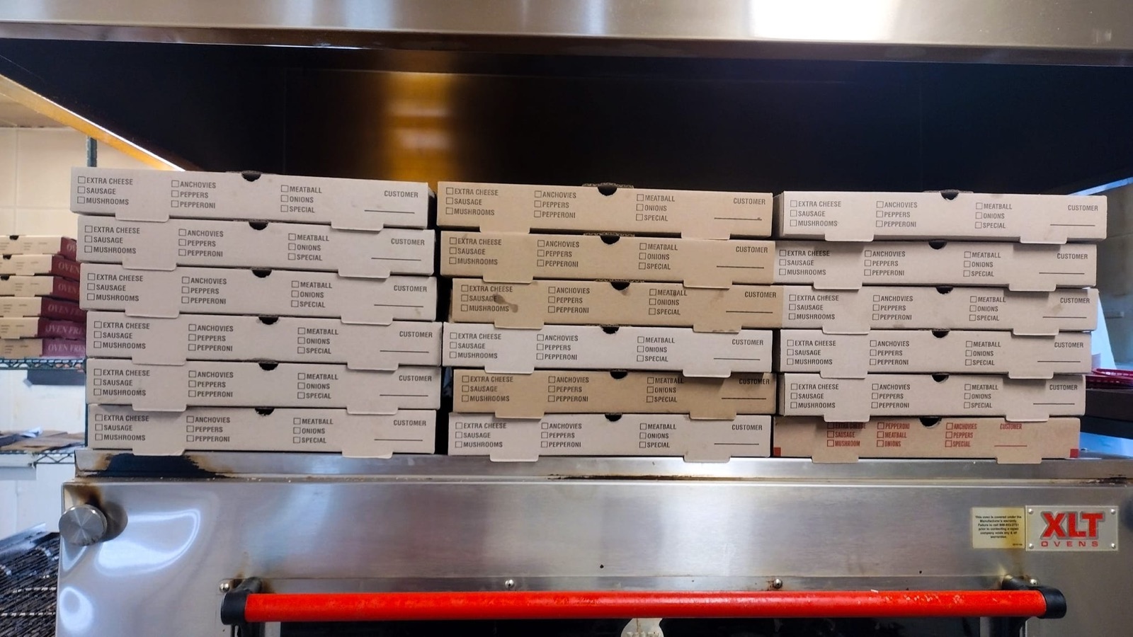 Stacks of pizza boxes lined up on top of the pizza oven