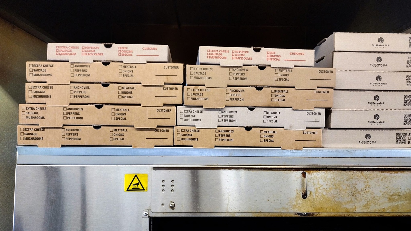 Brown pizza boxes stacked five high on a steel shelf
