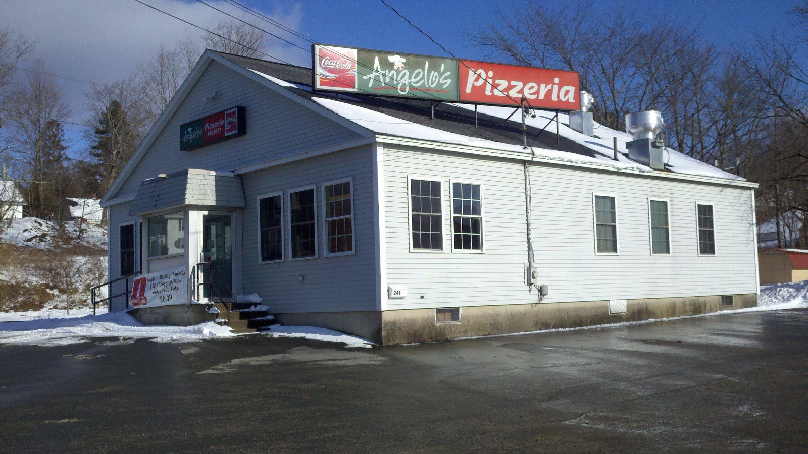 Angelo’s Pizzeria’s white clapboard building in winter, with the rooftop sign reading Coca-Cola, Angelo’s, Pizzeria